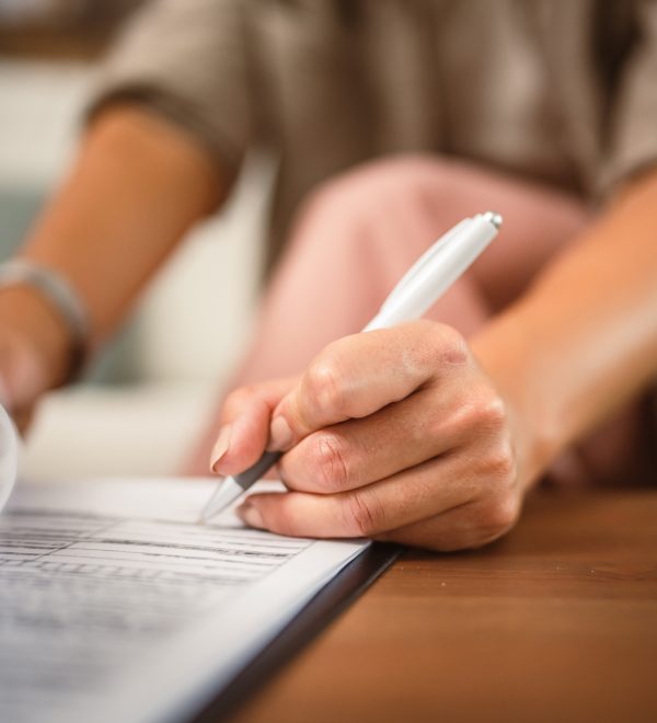 Close up of a woman holding a pen and signing the closing documents for her home purchase in Nassau County.